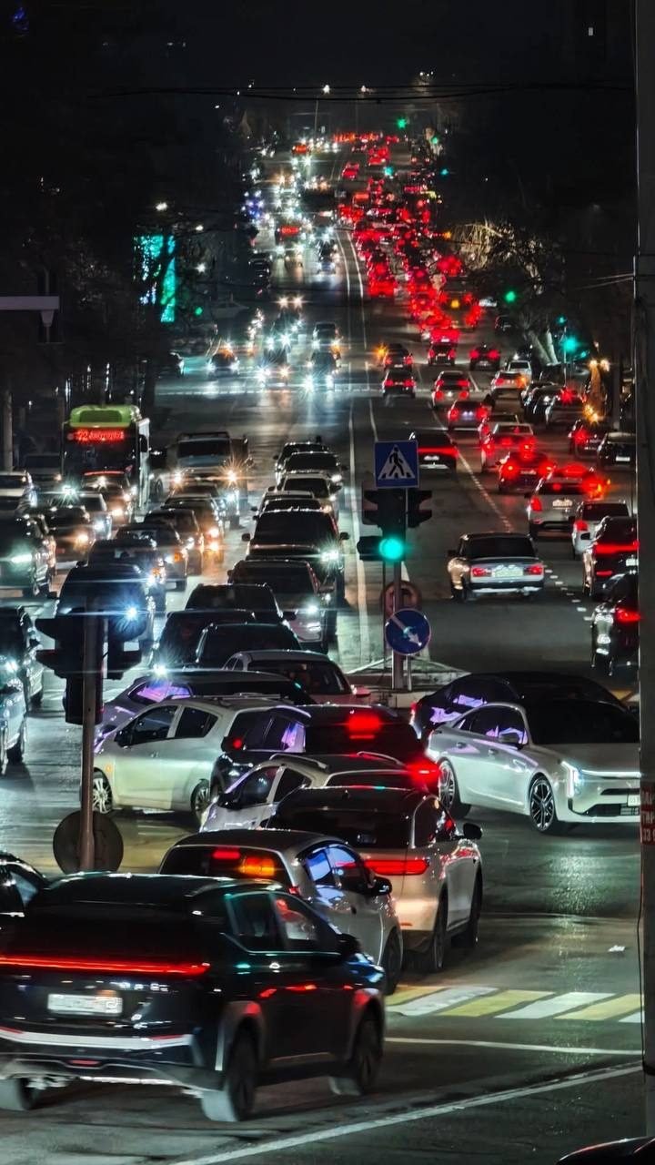 Avenida iluminada de noche con cientos de carros y semáforos en verde